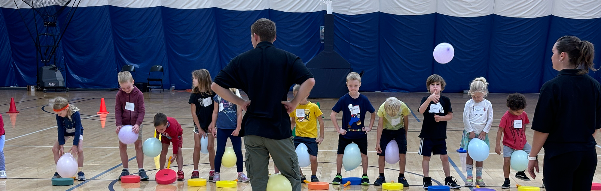 A group of children play in a gym with their teacher.