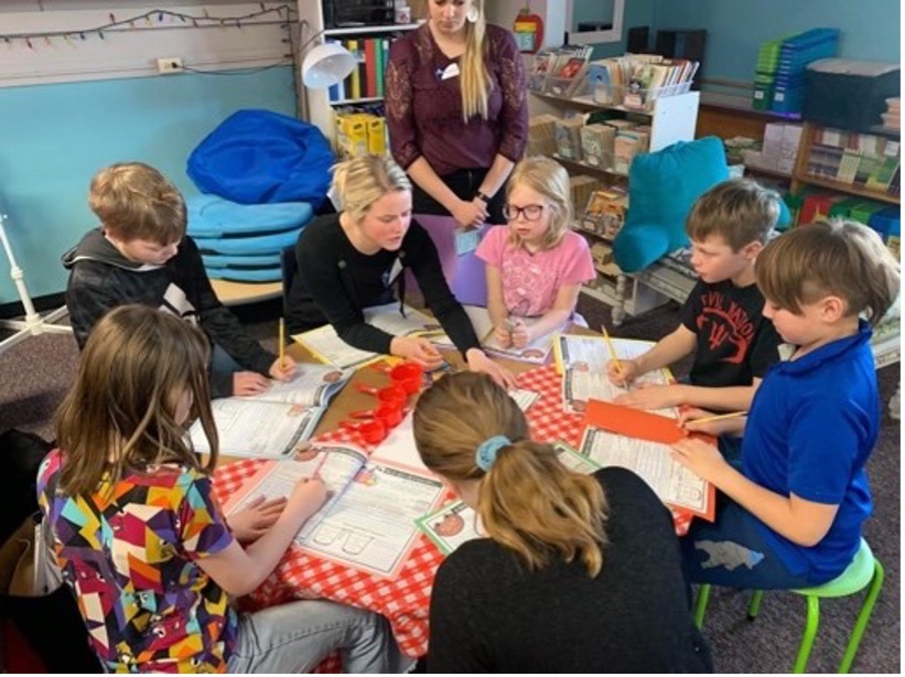 Two rural teacher candidates with young students around a table