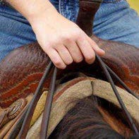 Person on a horse holding reins togther with one hand and they have all of their fingers through the loop