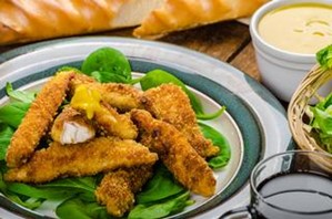 A plate of chicken fingers on a bed of spinach with a side of honey mustard. 