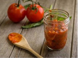 A jar of Easy Marinara Sauce next to a wooden spoon and two tomatoes.