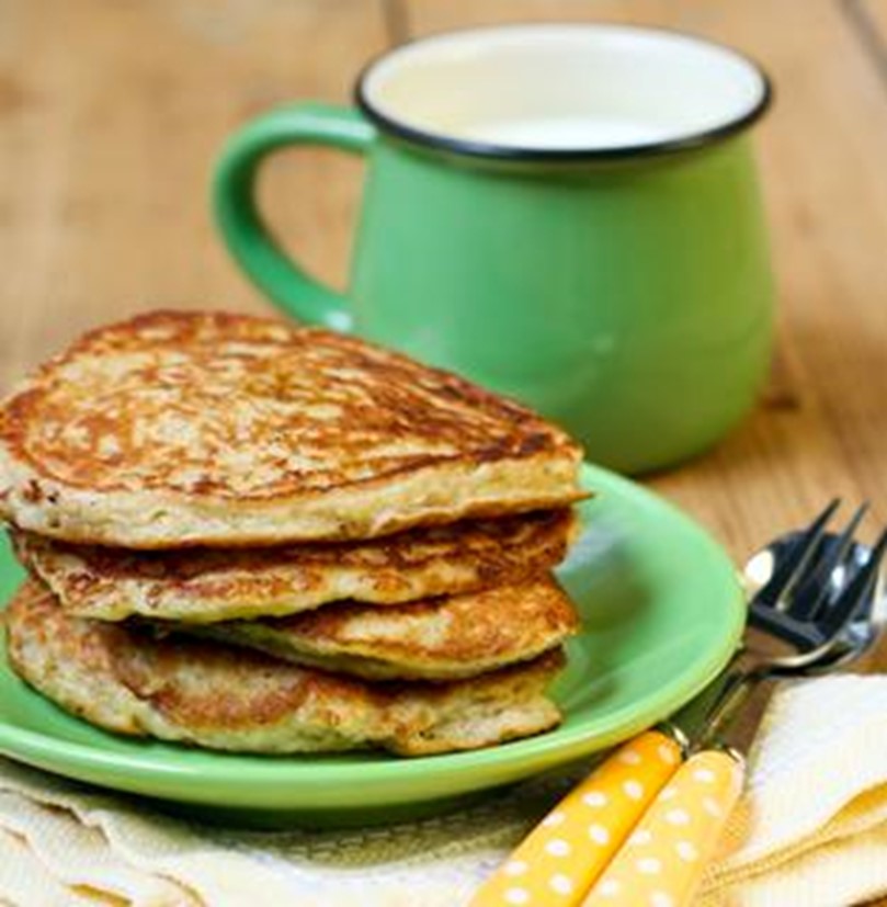 An image of four oatmeal pancakes in a stack on a green plate next to a green mug.