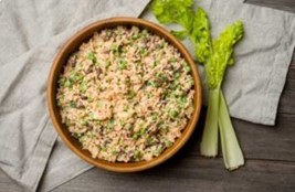 An image of rice salad in a brown bowl on top of a white linen and next to two sticks of celery.