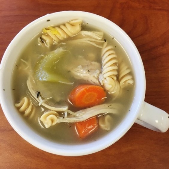 An image of rich turkey vegetable and noodle soup in a white mug.