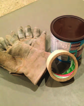 A pair of tan, thick, leather gloves sits on a table next to a can with a lid and a roll of white masking tape.