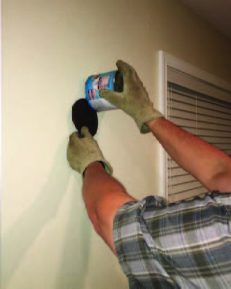 The gloved hands work together by sliding the lid of the can against the wall to push the bat into the can that's covering it.