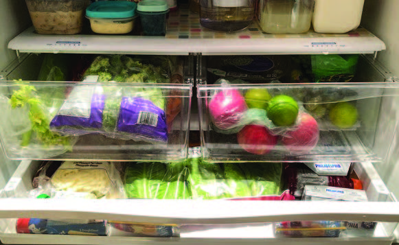 A fridge is open to display that it is filled with food, organized in draws and on shelves.
