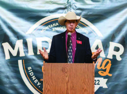 Jim stands at a wooden podium with a microphone and speaks.