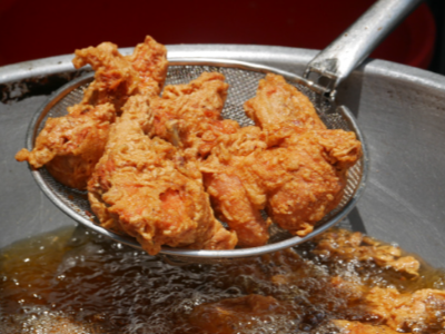 Crispy fried chicken is being lifted out of a pot of hot cooking oil with a long-handled strainer.