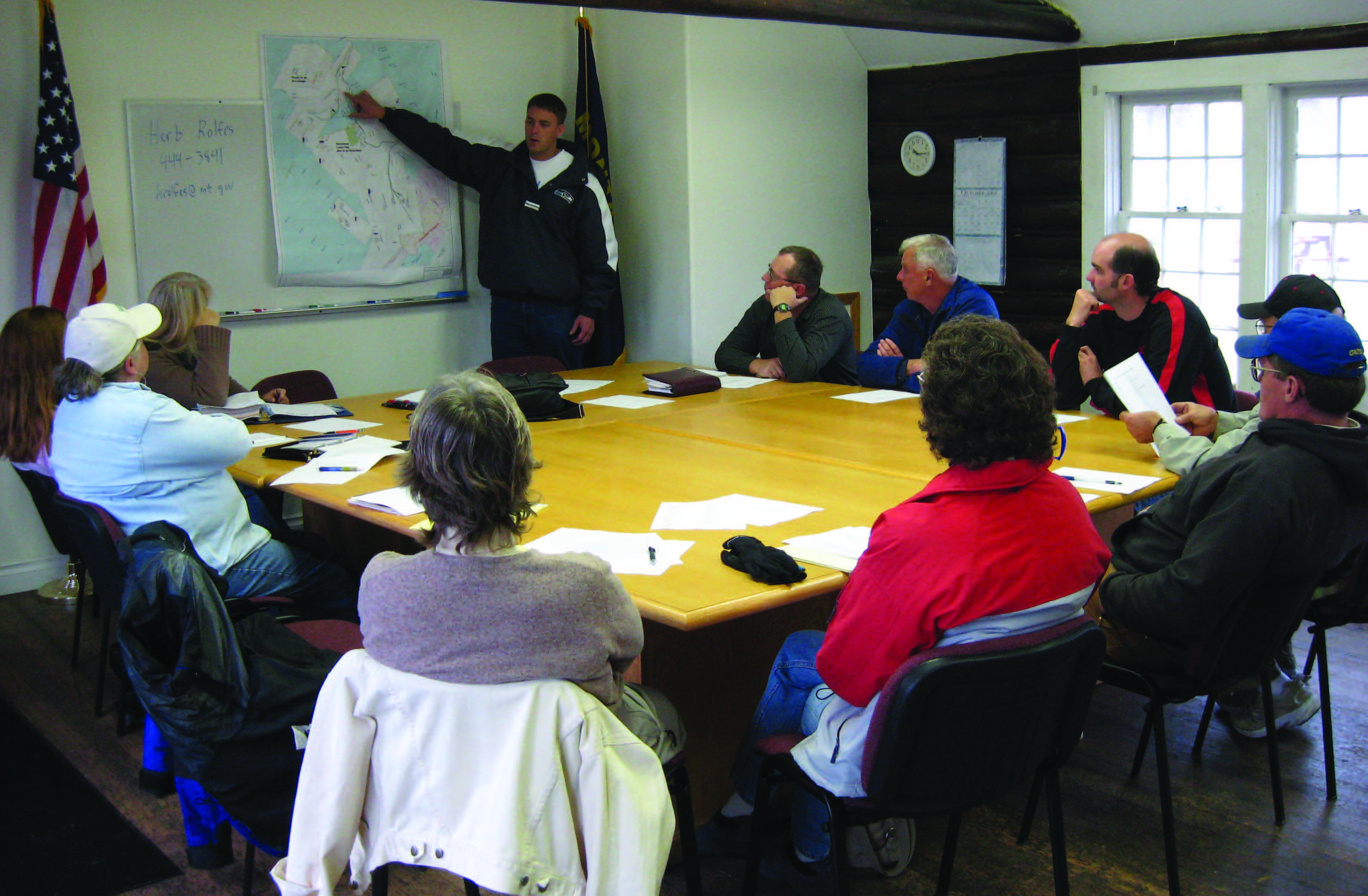 a local board meeting around a table with a presenter pointing to a map