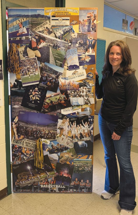 A woman stands next to a classroom door covered in MSU Bobcat posters and decorative items.