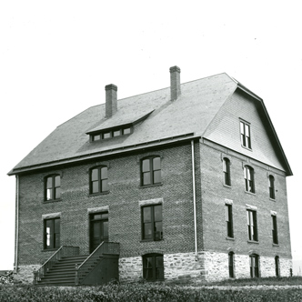 Taylor Hall is a square building made of brick with four floors and two chimneys.