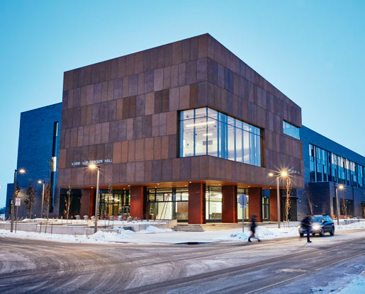 Purposefully rusted steel paneling, grey brick and windows form Norm Asbjornson Hall, a modern rectangular building on Montana State University's Bozeman campus. Windows wrap around the corner of the building on the second floor.