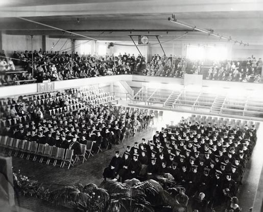 A black-and-white photo of Montana State University's commencement ceremony in 1935. The ceremony was held in Romney Gym. The graduates are seated in rows on the gym floor while family, friends and guests are seated above in bleachers.