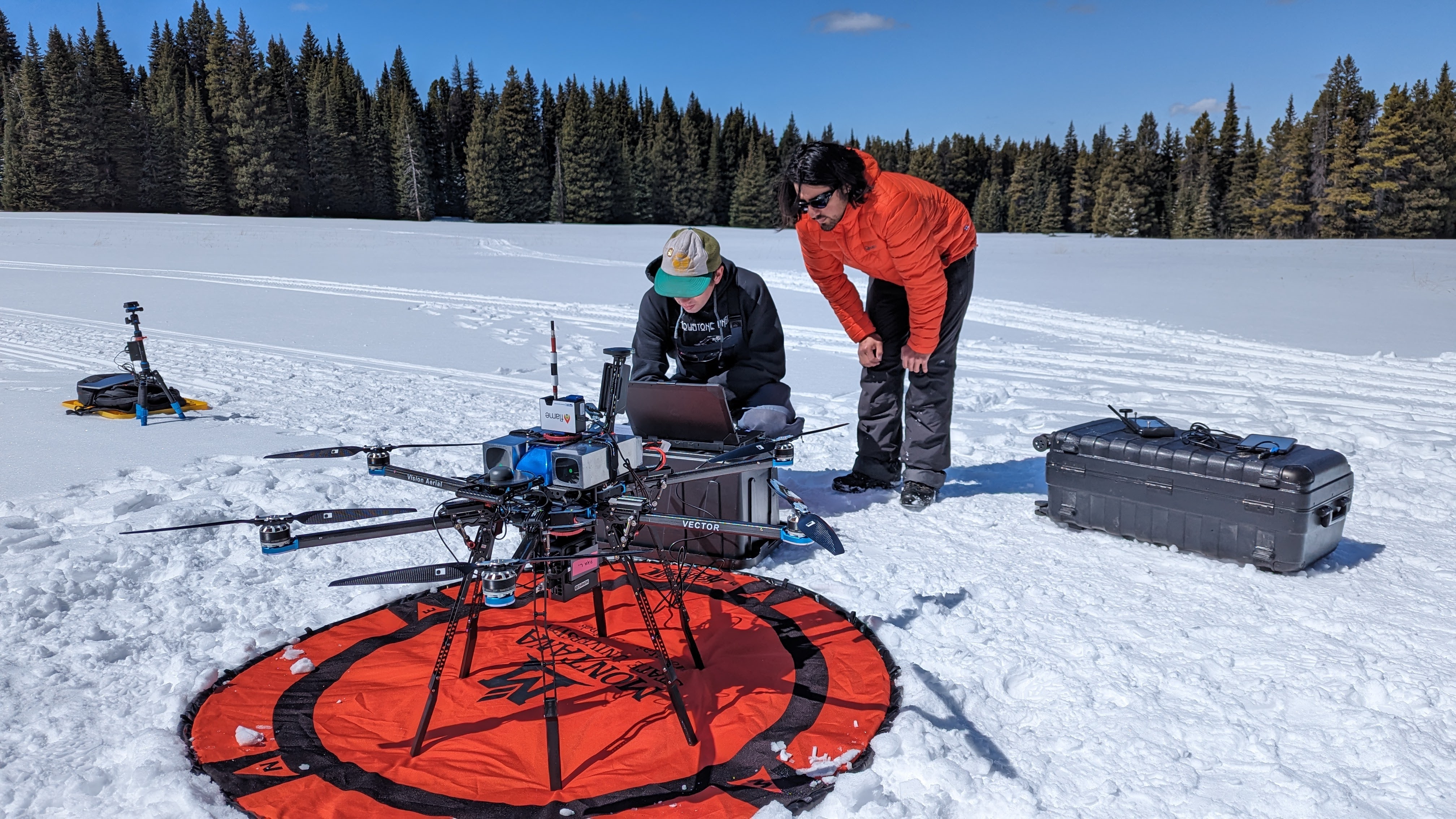 Vision Areal Vector drone ready to take off on a snow covered field. Two people behind it are checking the drone.