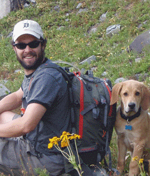 Anthony sitting in a mtn field with dog