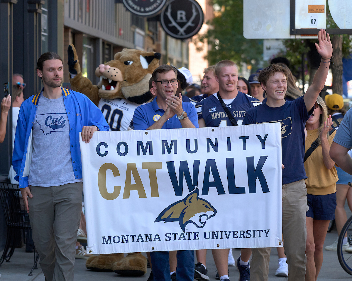 A group of people walking down a sidewal holding a Catwalk banner
