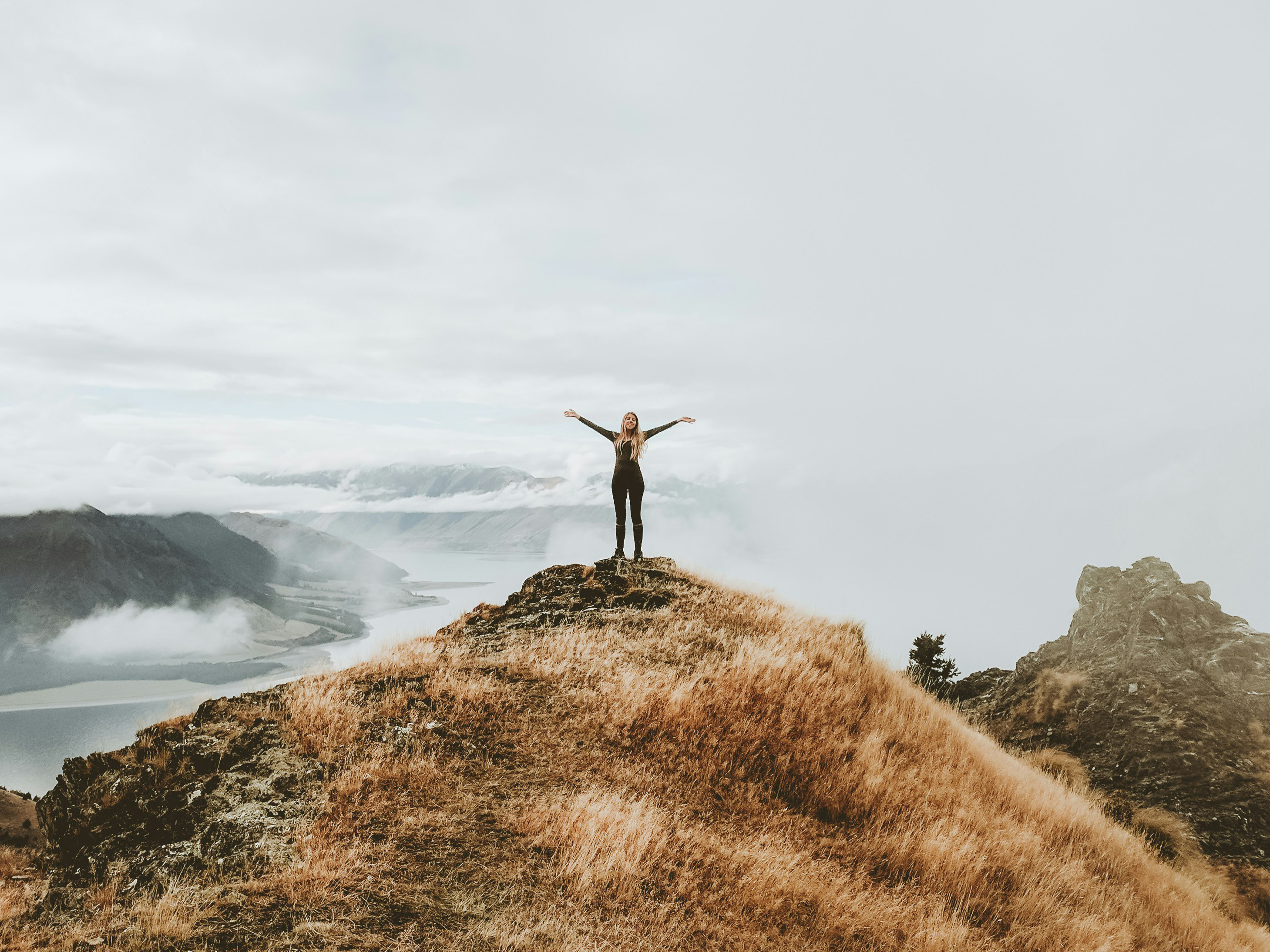 Stock image of a woman standing on a coastal hill with her arms up