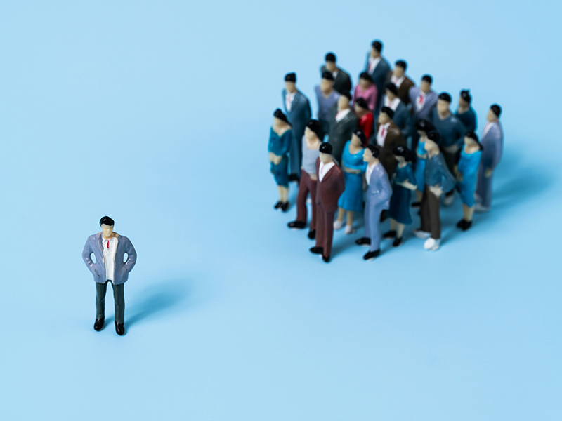 A single human apart from a big group of other humans of different races