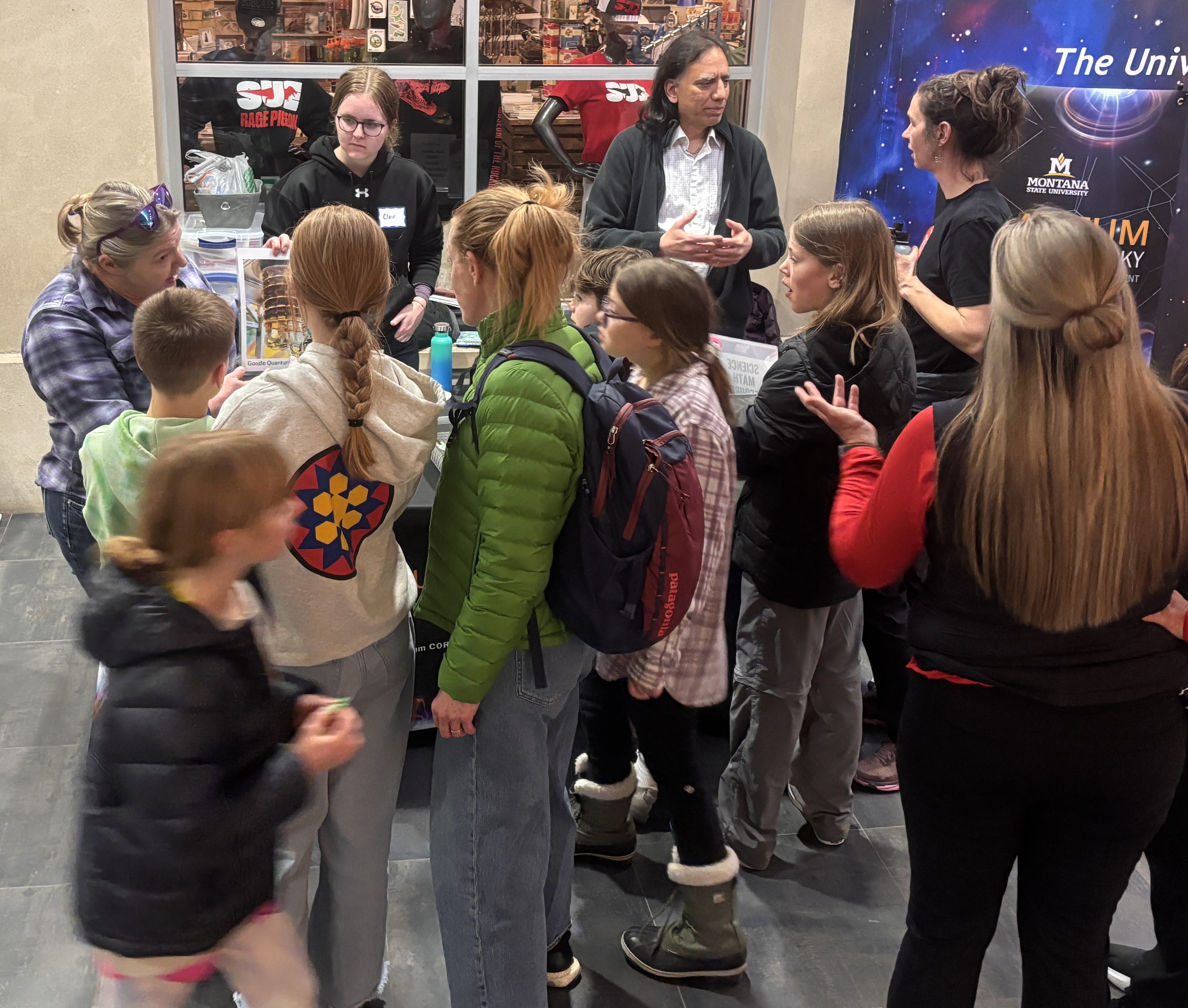 A crowd of students gathered around a booth at an outreach event.