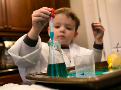A child filling a beaker with liquid from a pipette