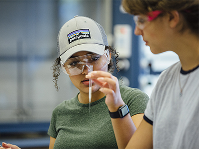 Student in safety goggles looking at a test tube