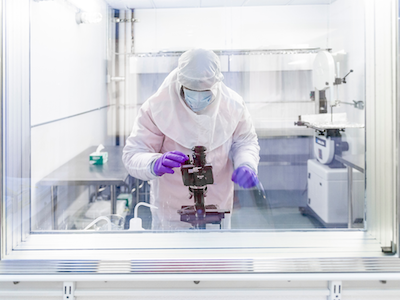 man wearing clean tyvec suit and face mask inside window of cold room